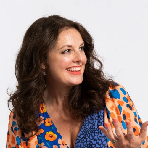 Image of a woman in a bright orange and blue patterned dress in front of a white background.