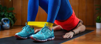 Woman exercising at home on mat with resistance band around ankles