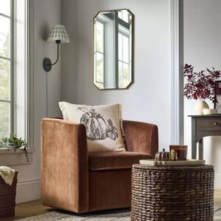 An orange armchair with a rectangular gold mirror hanging behind