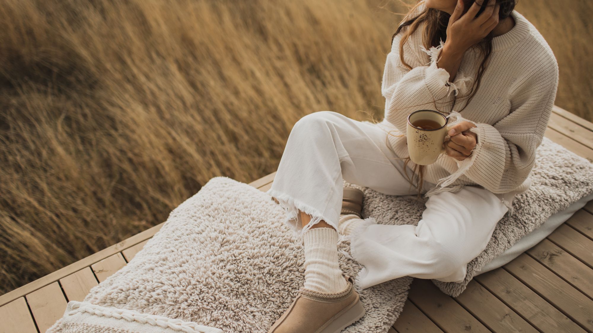 Hygge lifestyle: A woman drinking a cup of tea, wrapped up in cosy clothes and sitting on a blanket