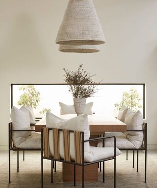 Neutral dining room with two low hanging pendants, dining chairs, wooden dining table, low rectangular window