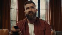 Jason Kelce sitting in living room trying to change the channel with remote control in YouTube TV ad