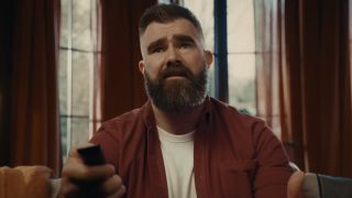 Jason Kelce sitting in living room trying to change the channel with remote control in YouTube TV ad