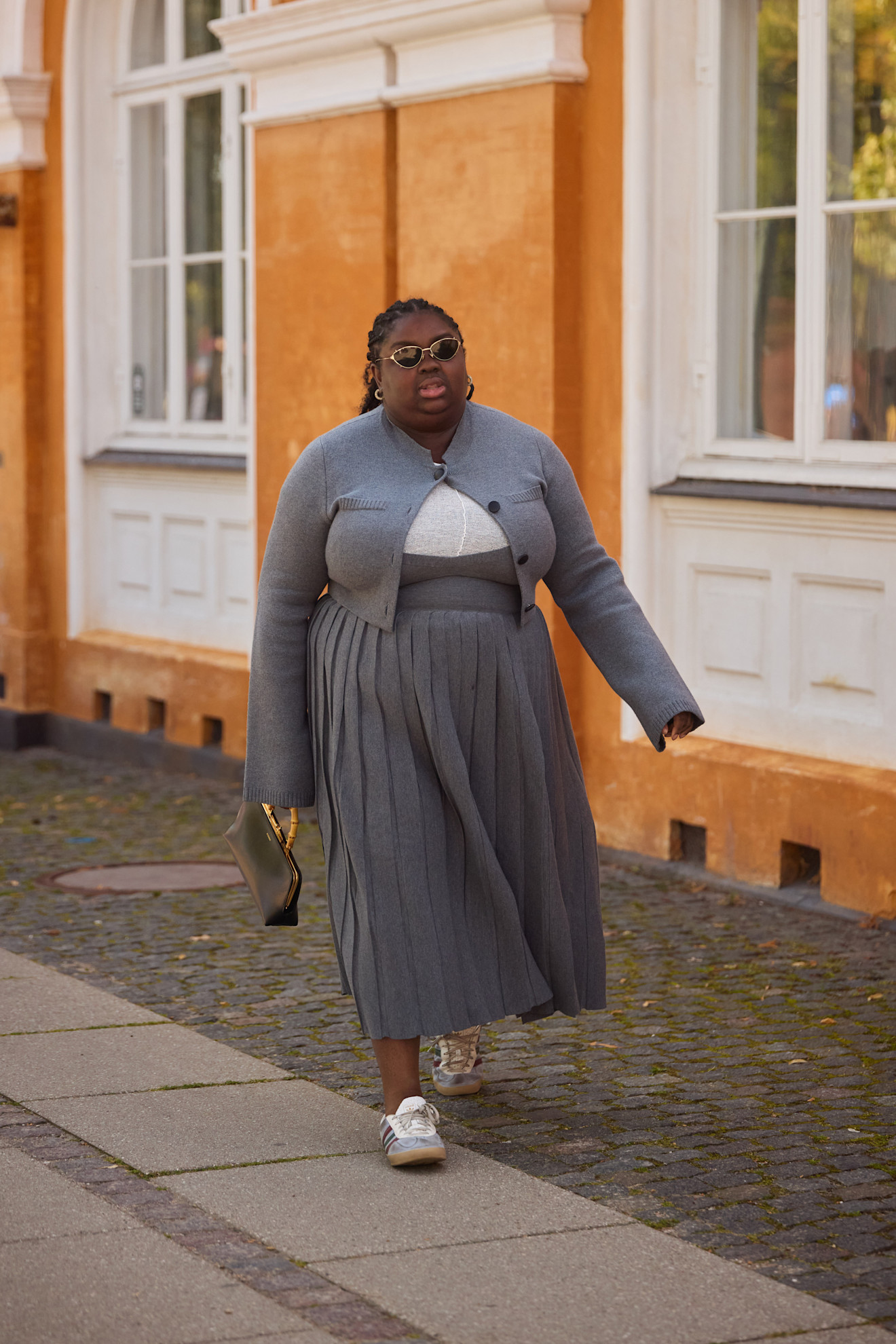 A woman wears sneakers and a gray dress with a sweater.