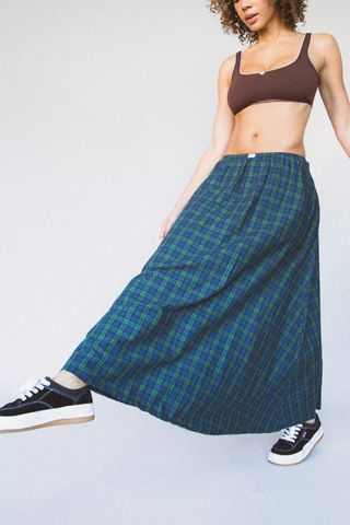model wears green plaid skirt and black sneakers with brown bra