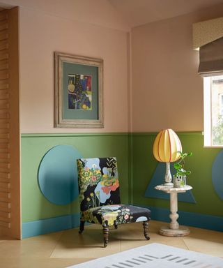 A living room area with a black floral chair, pink and green walls, and a framed abstract painting