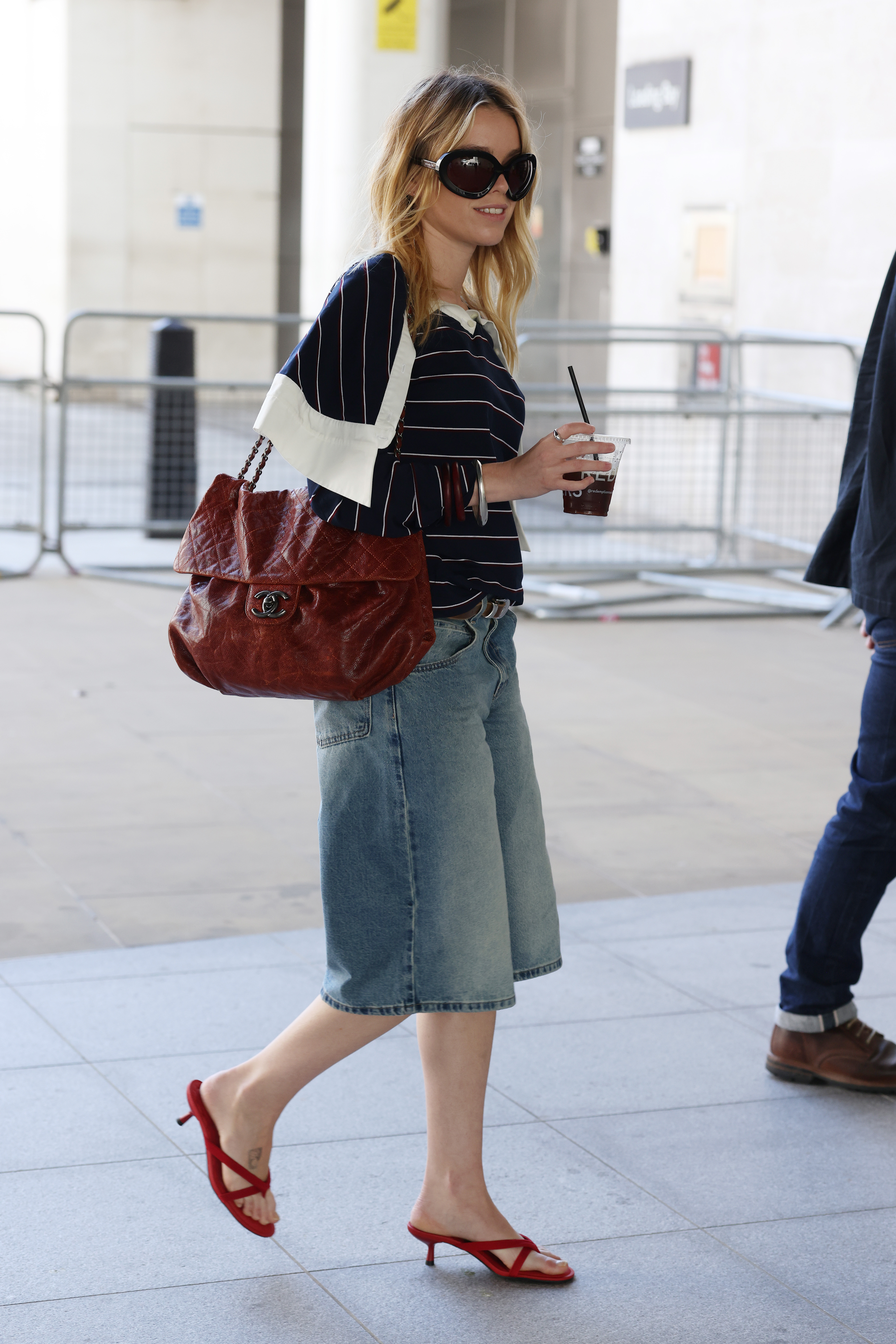 Milly Alcock styled the heeled flip-flops trend with denim Bermuda shorts and a Chanel Maxi Flap Bag June 19