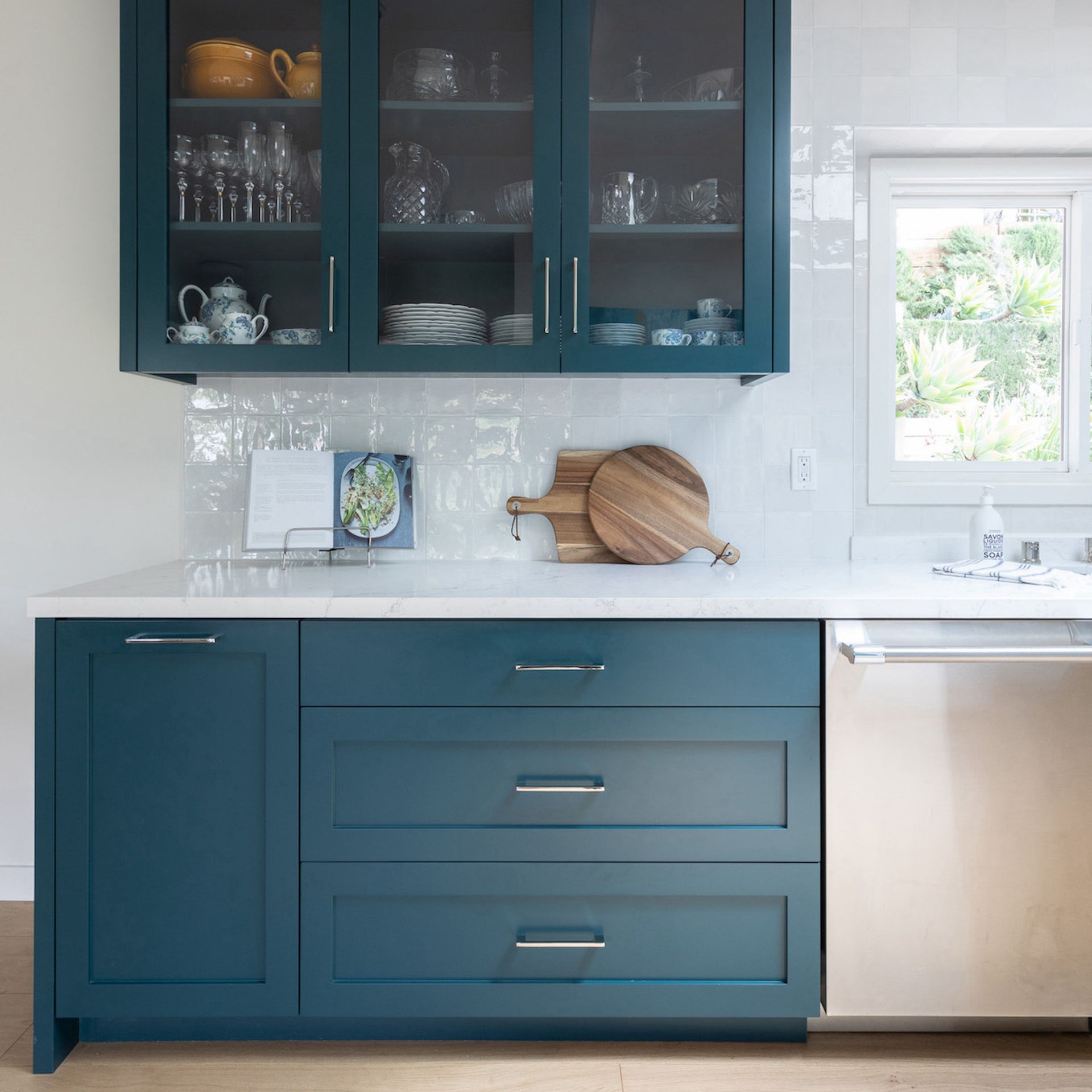 Area dapur dengan kabinet teal, countertop putih, dan backsplash