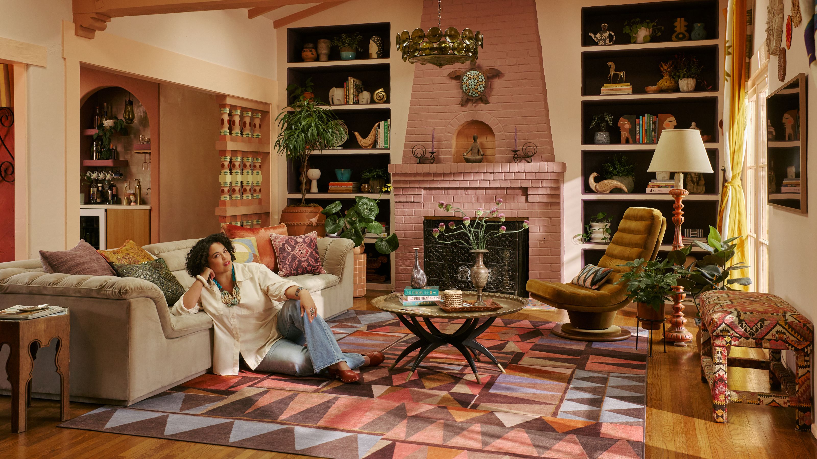 Ruggable x Jungalow rug collab with pink brick fireplace, geometric rugs, decorated shelves, gray sofa, potted plants and Justina Blakeley 