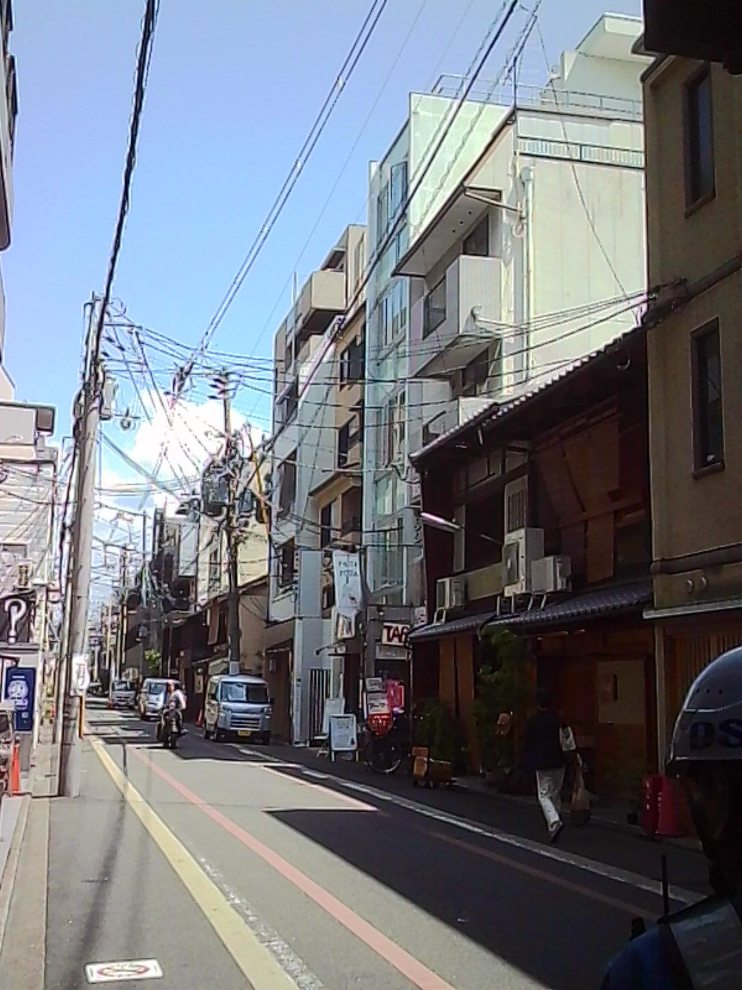 Quiet Japanese side street with modern buildings, overhead cables, and parked vehicles.