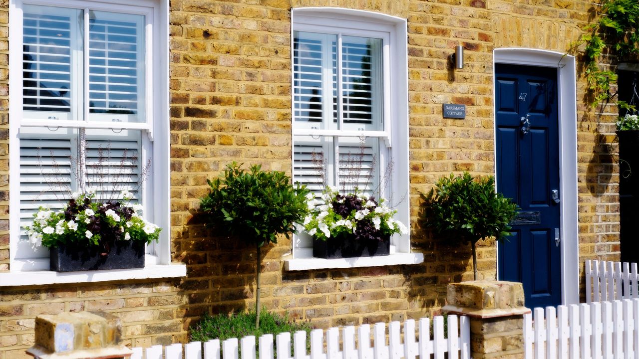 Exterior brick house with a blue front door, window boxes, ornamental trees and a white picket fence