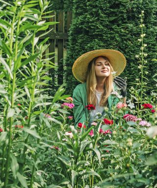 Gardener in sun hat enjoys smelling flower in garden