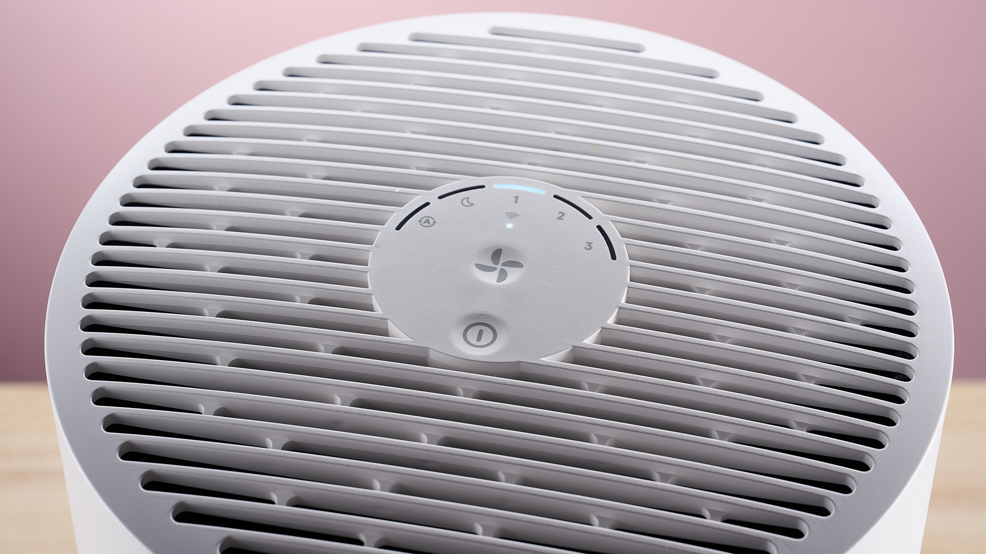 A close-up of the top of Blueair air purifier on a wood surface against a pink background.