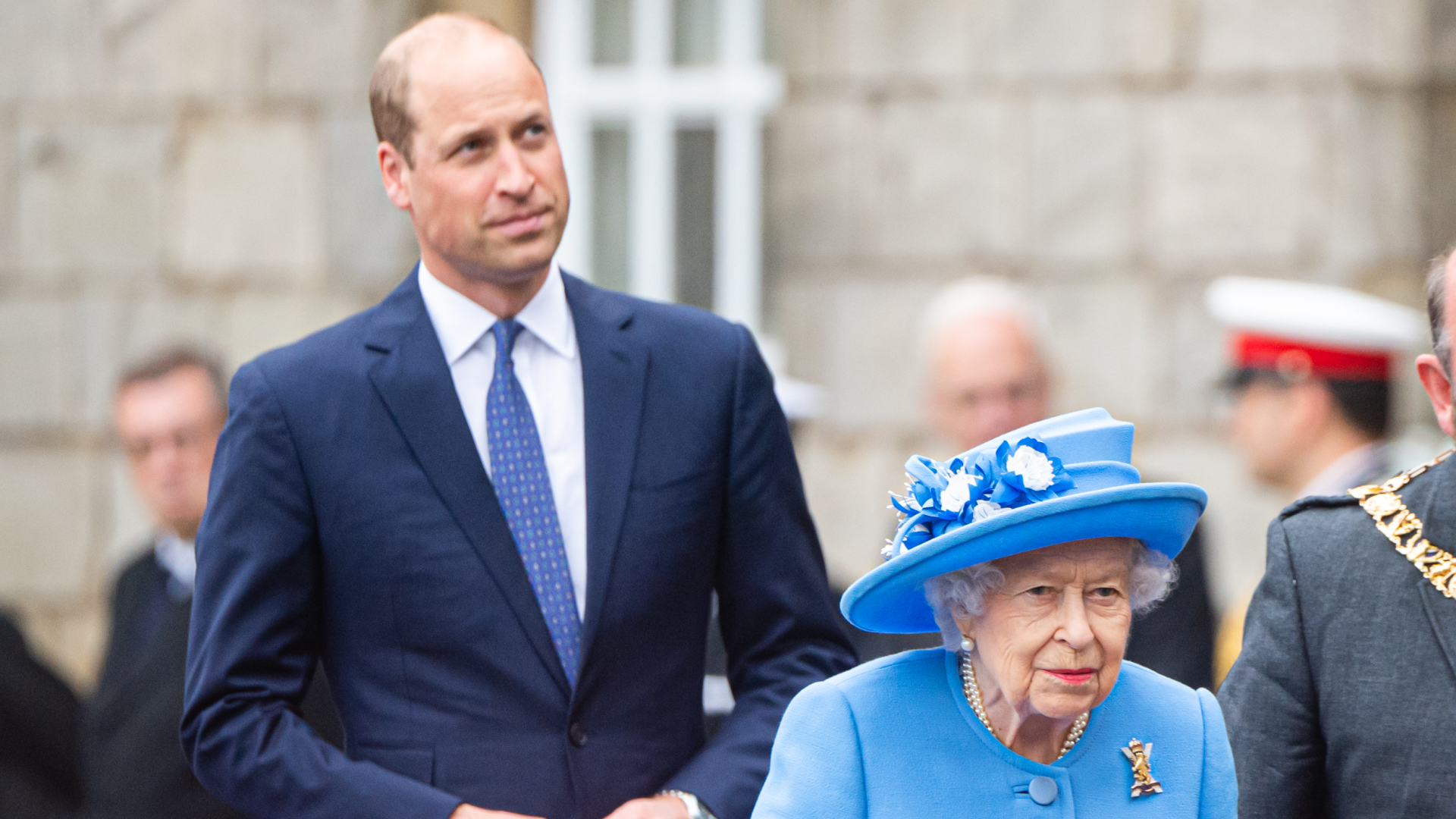Prince William wearing a blue suit walking behind Queen Elizabeth, dressed in light blue