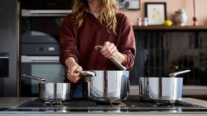 Woman wearing maroon jumper cooking with three stainless steel saucepans with foldable handles