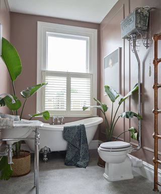 A pink bathroom idea with industrial style sanitaryware, freestanding white bath and copper towel rail