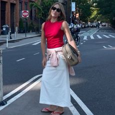 Anna wears a red top, white skirt, flip-flops and a beige bag.