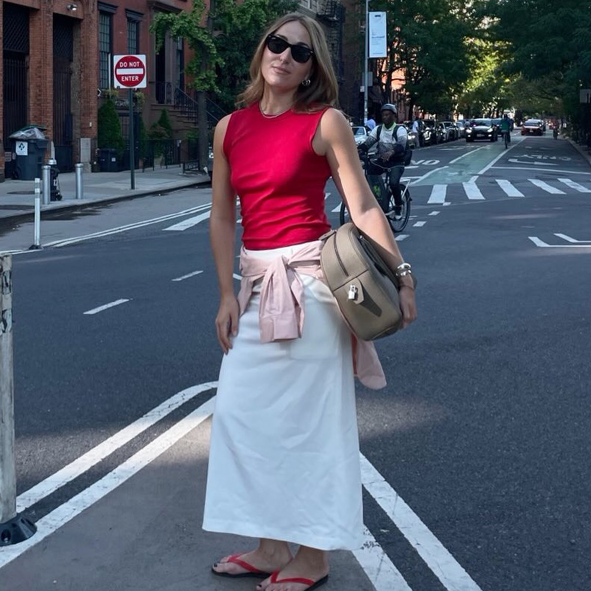 Anna wears a red top, white skirt, flip-flops and a beige bag.