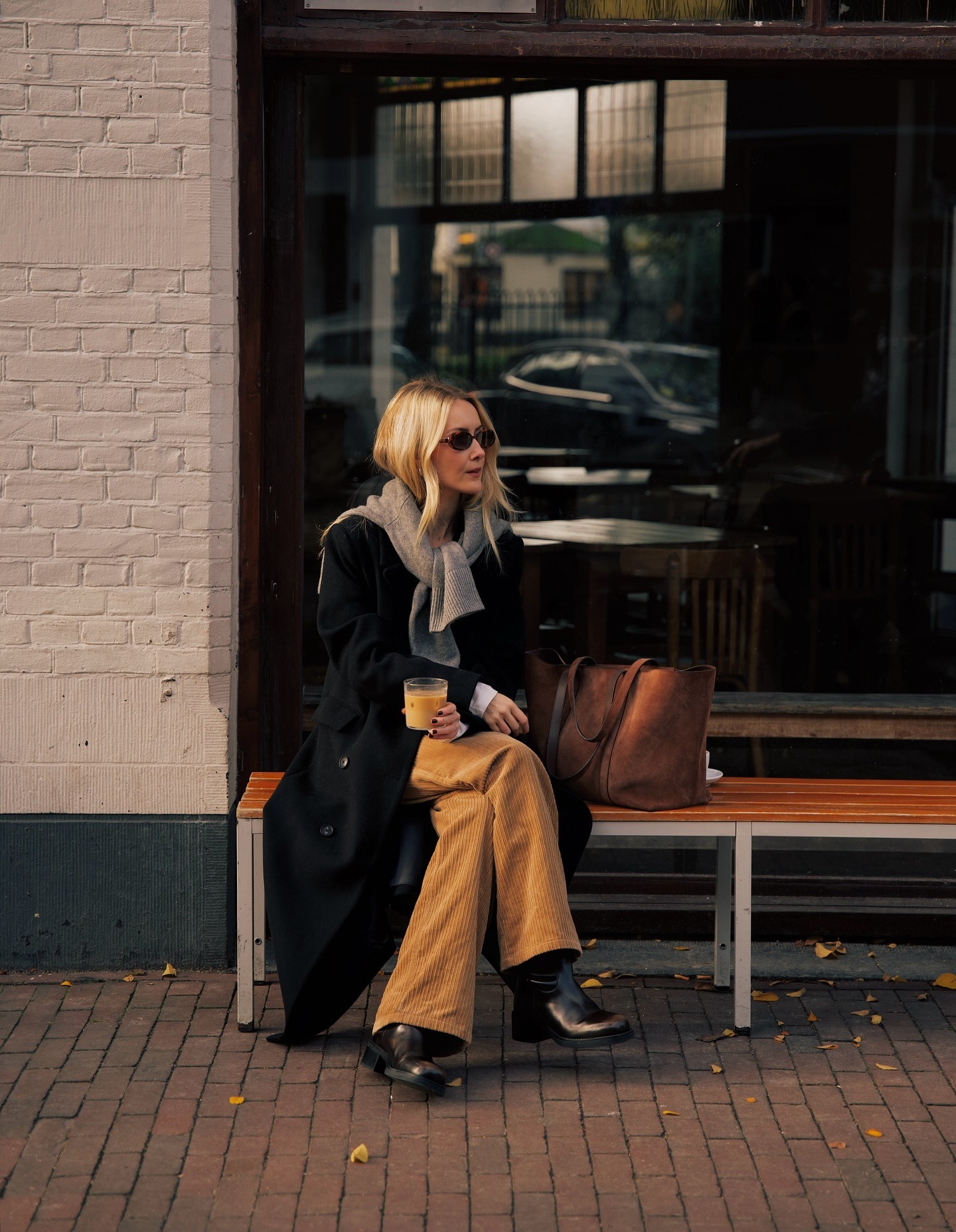 Chloe wears a black coat, gray sweater, corduory jeans, and black boots.