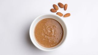 Almond nut butter in ceramic bowl with scattered almonds round the outside