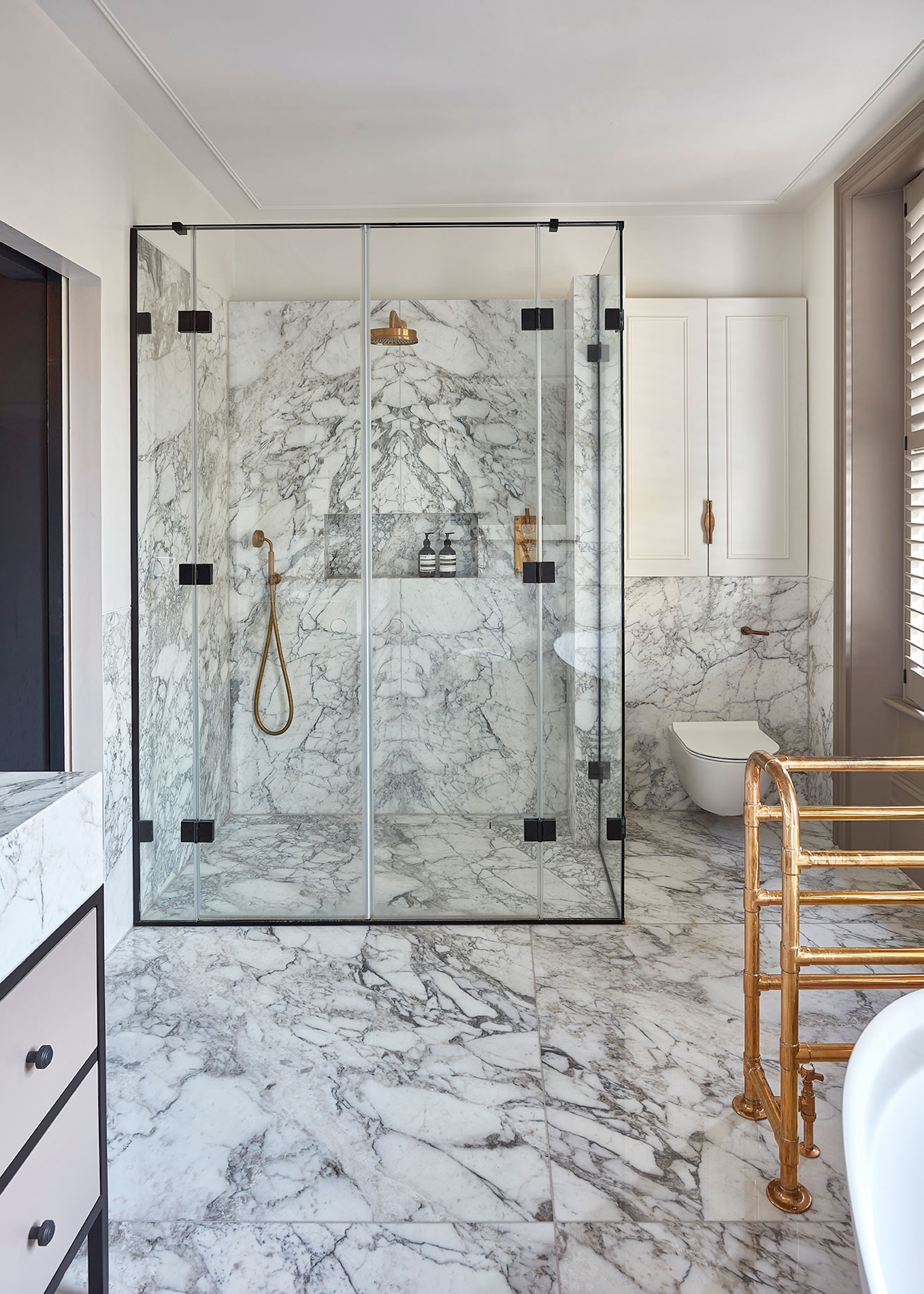 a classic bathroom with marble floors and walls and a large shower enclosure, storage cupboards and brass fittings