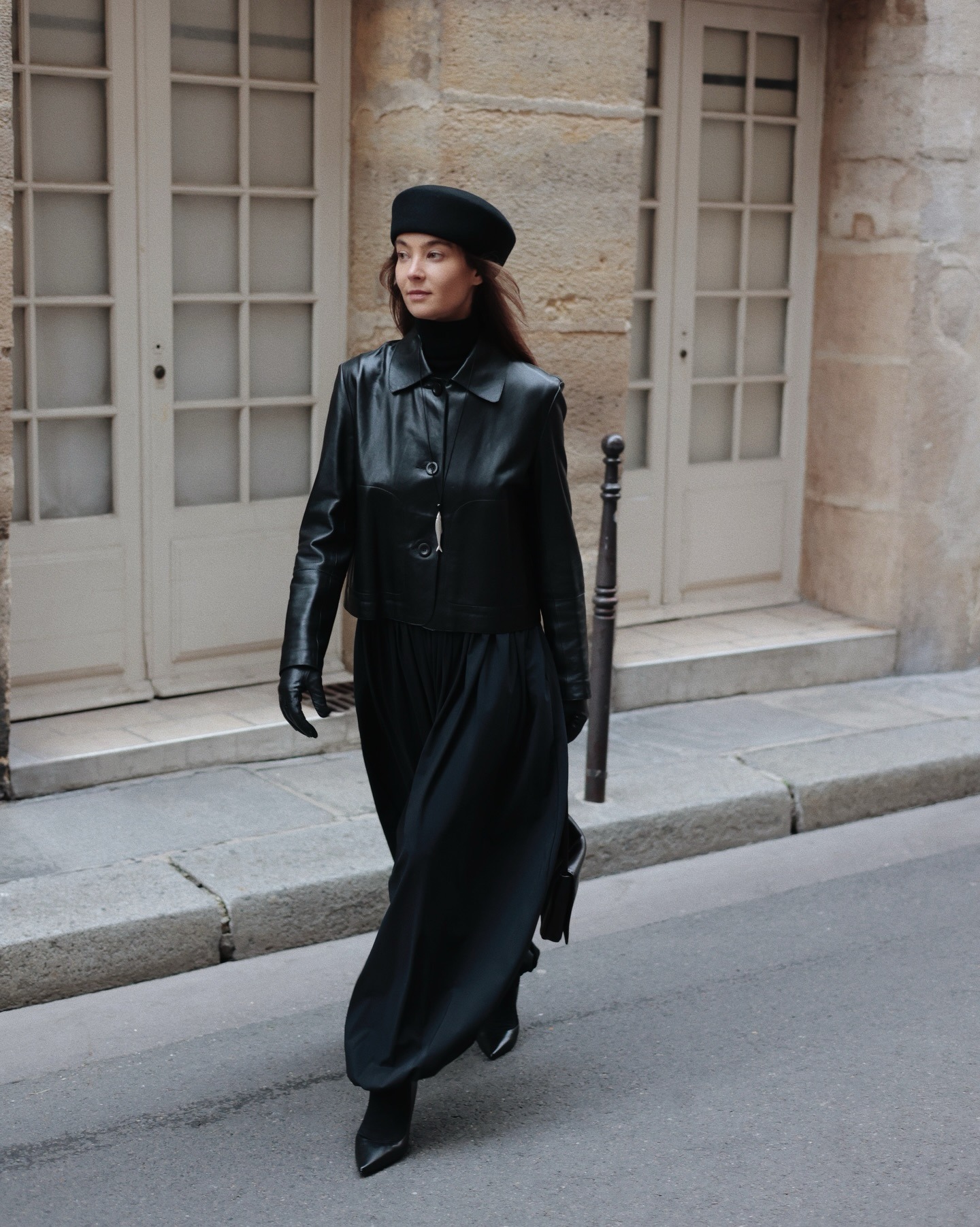 Woman wearing cropped black leather jacket with black balloon trousers and a black pillbox hat.