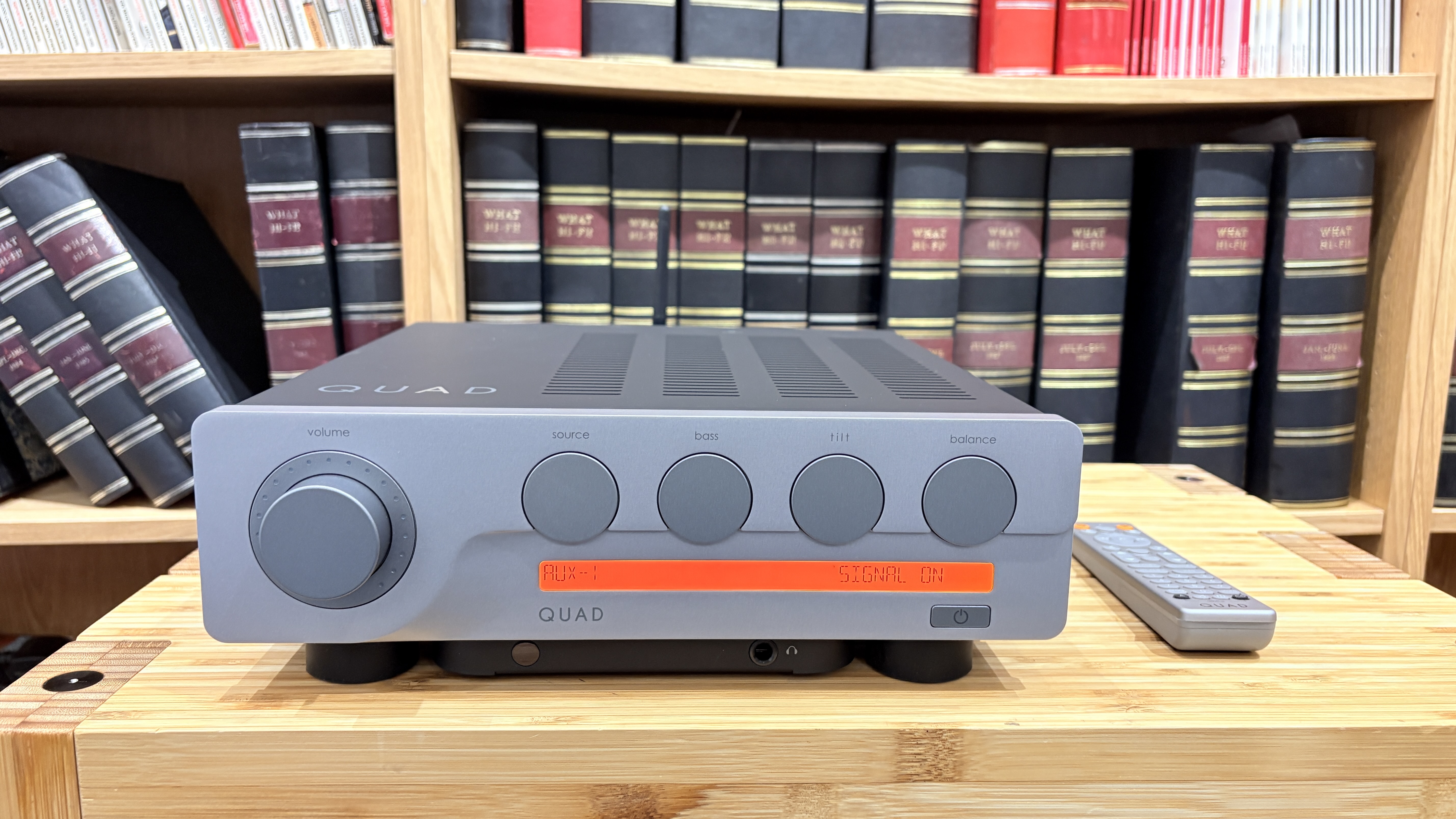 Quad 3 amplifier and remote on wooden shelf with bookcase in background