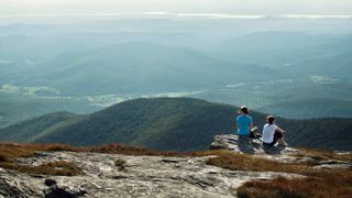 Rear view of friends sitting on cliff against mountains