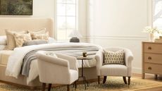 neutral farmhouse bedroom with an upholstered cream bed with layered bedding and two striped armchairs with a wooden dresser