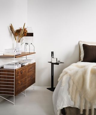 white minimalist bedroom with modular cabinet with white metal, modern black side table, bed with textured bedding and throws