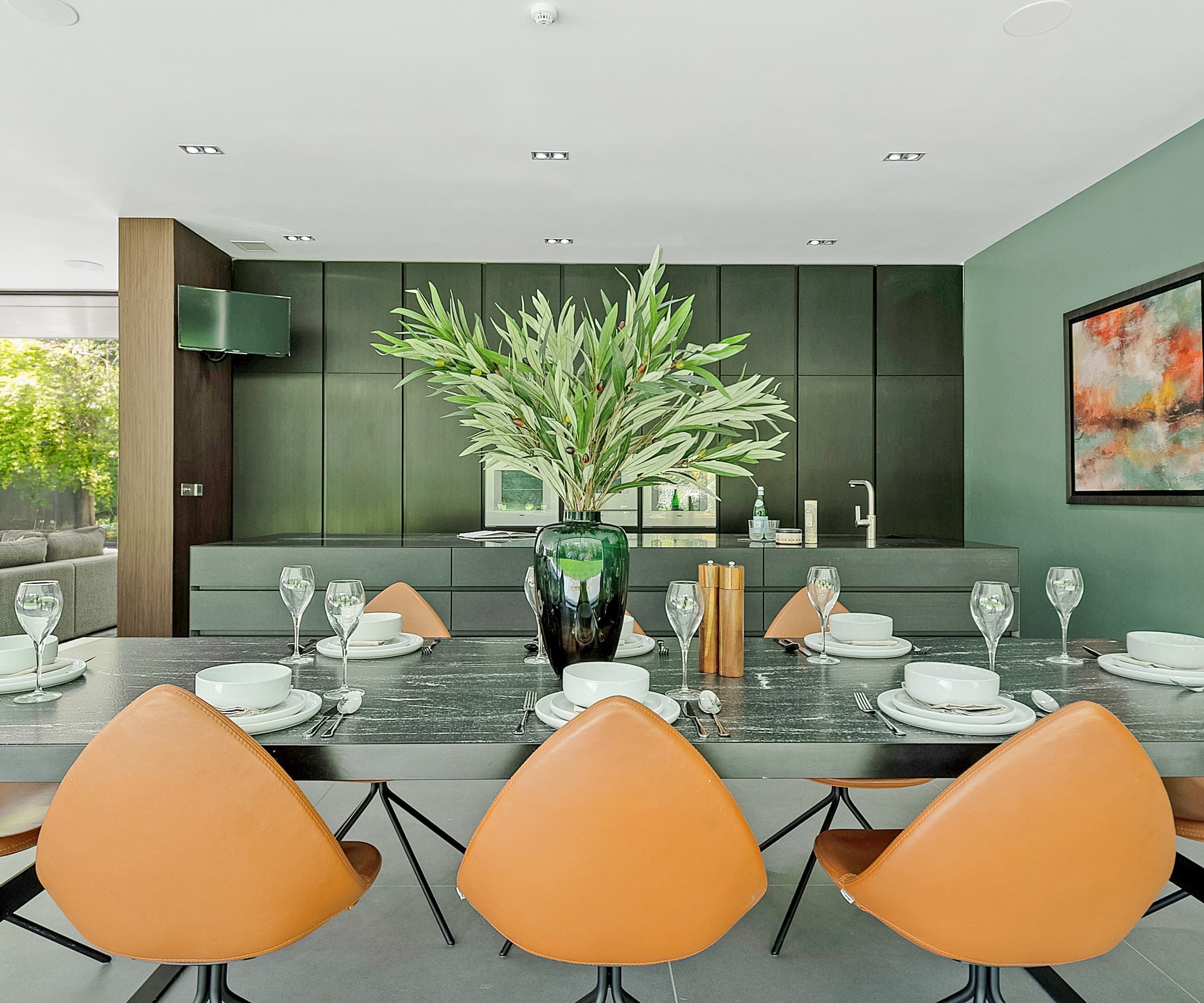 A kitchen table with orange chairs next to a kitchen with a green island and cabinets