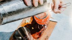 overhead shot of an orange cocktail being strained into a cocktail glass