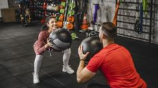 two people exercise their lower bodies with weighted medicine balls