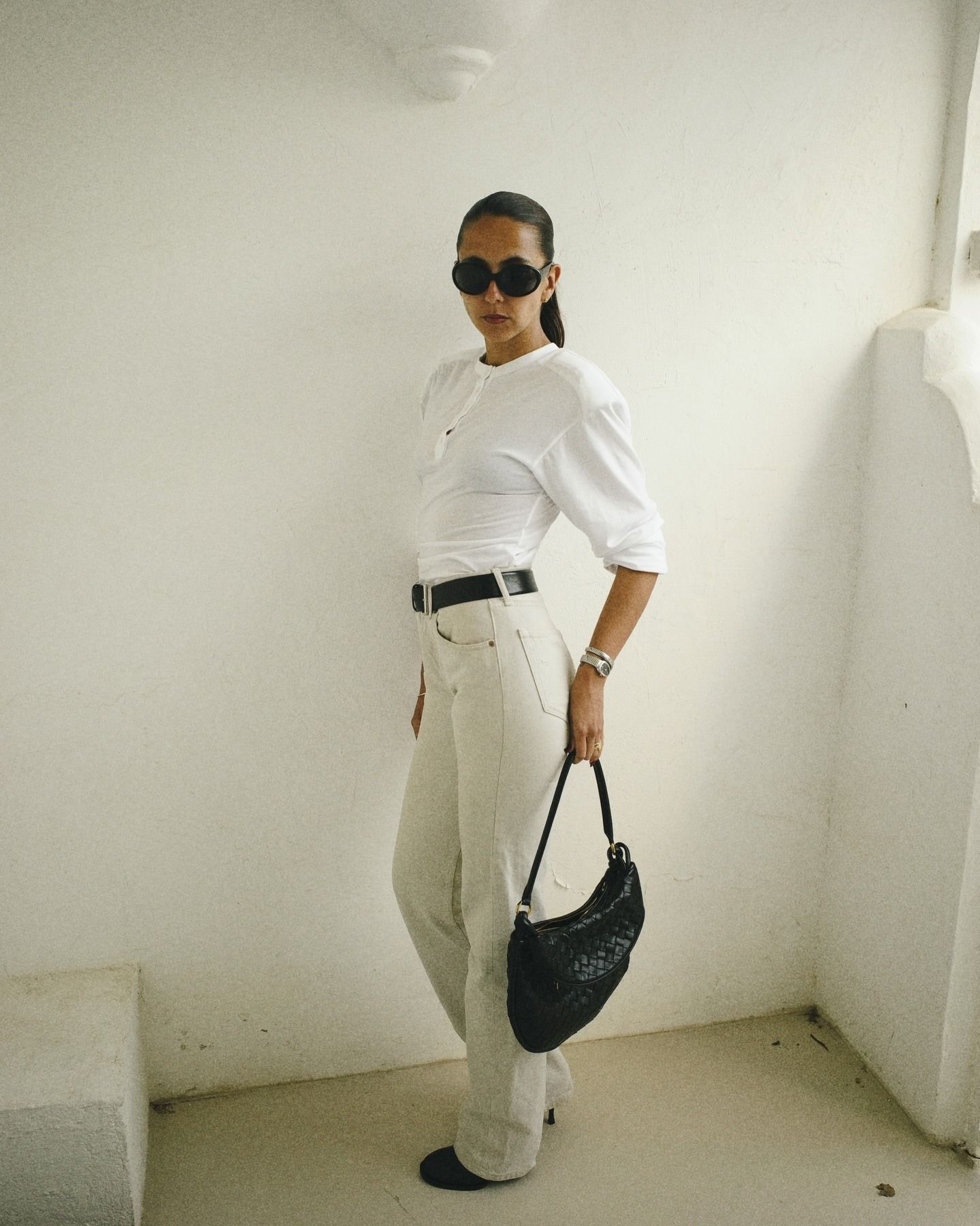 hanna wears a white tee, black belt, white jeans, black boots and a black bag.