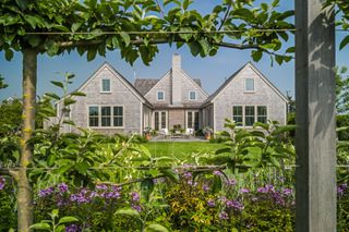 The exterior of a New England-style house features a thriving garden and wooden paneled walls.