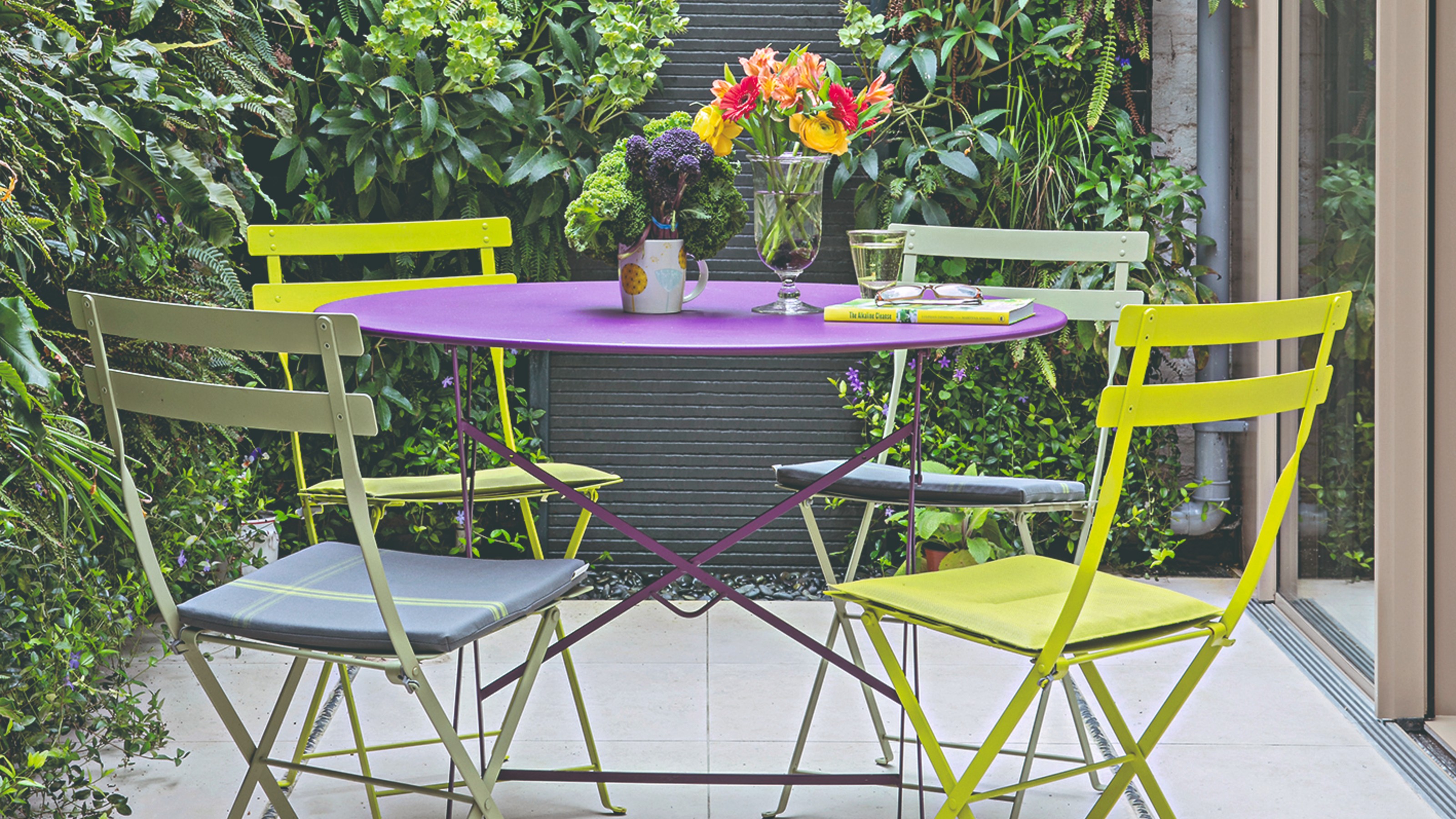 A small garden with a multi-coloured bistro set adorned with two vases of flowers