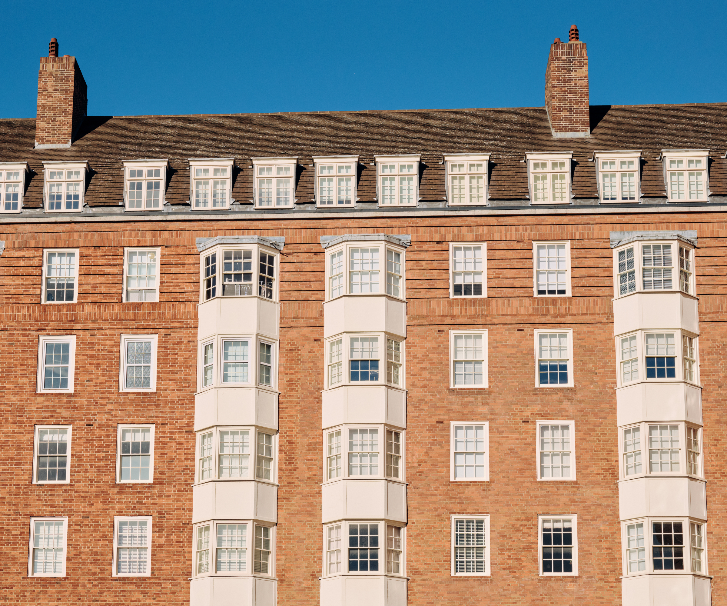 tall block of terraced flats with brick facade, white clad bay windows and tiled roof