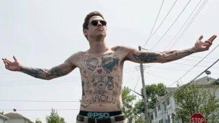 Pete Davidson wearing sunglasses, showing off his many tattoos with arms wide open in The King of Staten Island