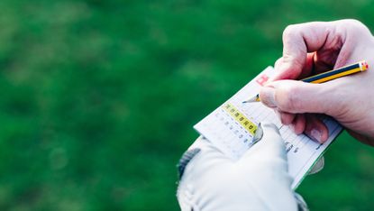 A man marks a score on his golf scorecard.