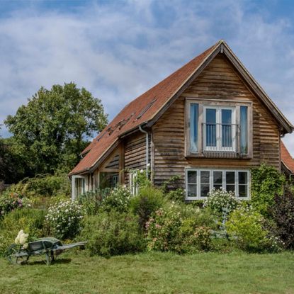 Exterior of a timber clad, oak framed house with lawn and flower beds. A new build oak framed two bedroom house in the New Forest in Hampshire, home of Elizabeth and Derek Sandeman