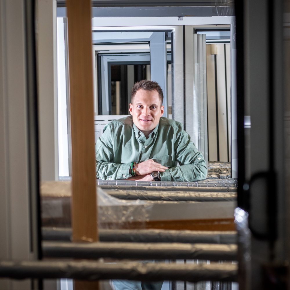 male wearing green shirt standing at end of a pile of doors and windows