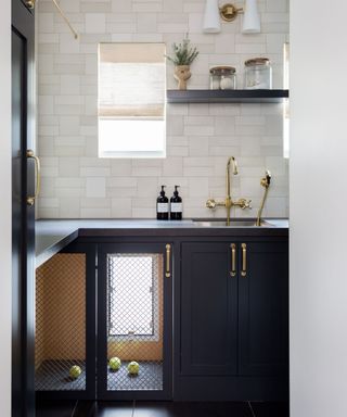utility with dark gray cabinets and built-in under counter dog crate with tennis balls