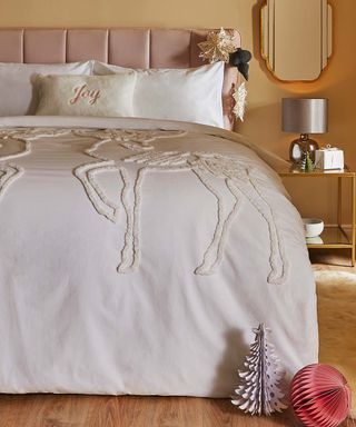 A feminine bedroom scheme with raised reindeer motif bedding, metallic silver lampshade fixture, faux fur rug, and brass-framed glass side table