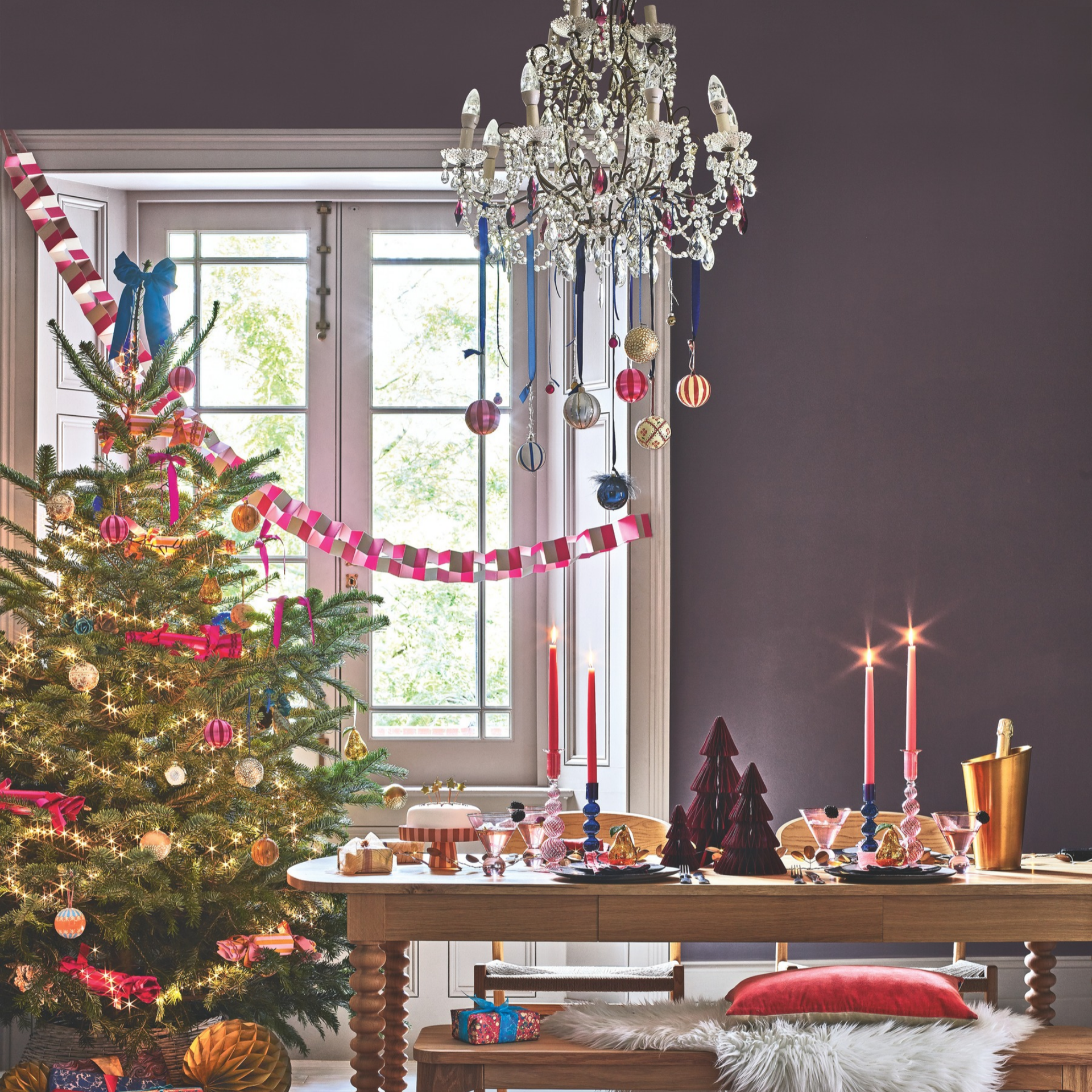 Maximalist Christmas dining table with paper trees, candles and ice bucket. A colourfully decorated tree is next to it.