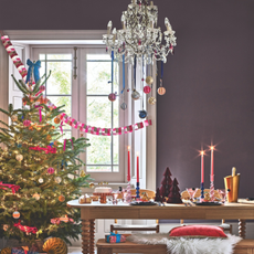 Maximalist Christmas dining table with paper trees, candles and ice bucket. A colourfully decorated tree is next to it.
