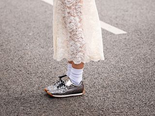 A street style image of a stylish person wearing silver sneakers with white socks and a white lace skirt.