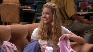 Phoebe sitting on the couch holding pink clothes in Friends