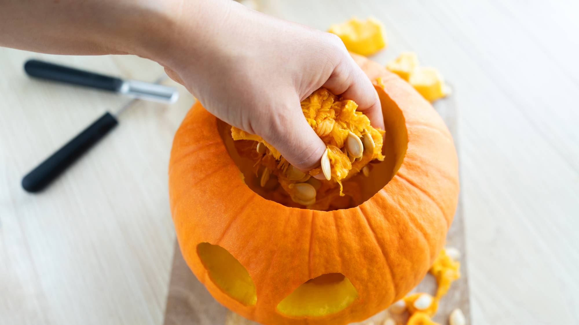 Hand reaching into a carved pumpkin to scoop out a fistful of stringy orange pulp and seeds.