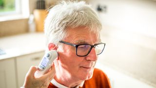 Older adult having temperature taken with an ear thermometer