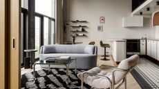 A spacious living room with white walls, a black and white rug, and gray furniture.
